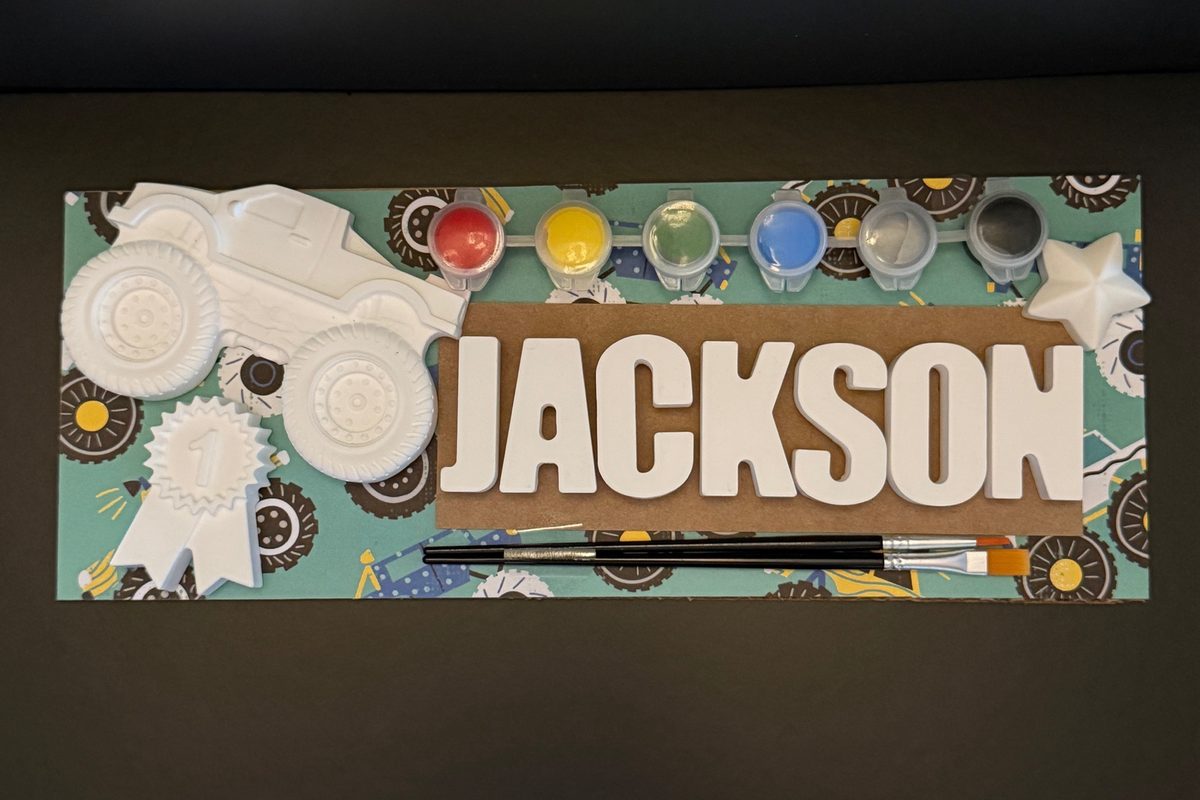 Custom name kit spelling JACKSON with a monster truck, first-place ribbon and star on a monster-truck board, six paints and two brushes.