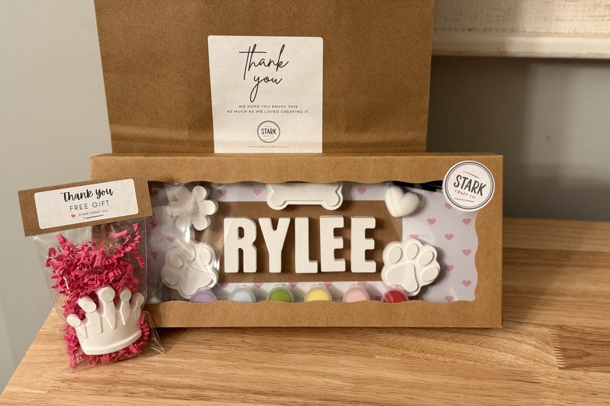 Custom name kit spelling RYLEE with paw prints, a bone, a heart and a flower, boxed in a kraft window box with a thank-you bag.